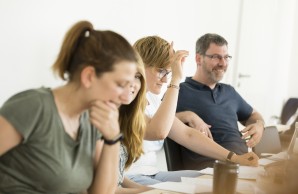 Menschen sitzen an einem Tisch und befinden sich im Austausch untereinander