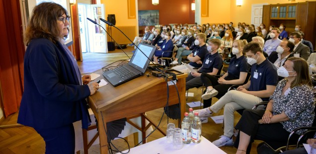 Frau Dr. Zimmermann steht in einem Raum voller Menschen an einem Rednerpult