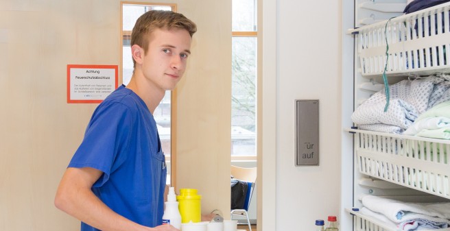 Junger FSJler schaut in die Kamera auf dem Weg in ein Patientenzimmer