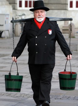 Wasserträger Hans Hummel ist an seiner schwarzen Tracht und dem Zylinder mit den zwei Wassereimern gut zu erkennen