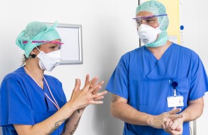 Dana Möller und Steffen Lamprecht mit Atem-, Gesichtsschutzmasken und grünen Tüchern über den Haaren desinfizieren ihre Hände