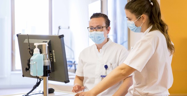 Dr. Louise Roggelin und ein Kollegin stehen nebeneinander ung Blicken auf einen Monitor. Beide tragen weiße Arbeitskleidung und einen Mund-Nasen-Schutz