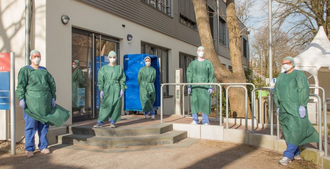 Mitarbeiter vor dem Gebäude der Atemwegsambulanz in Schutzkleidung und großem Abstand zueinander