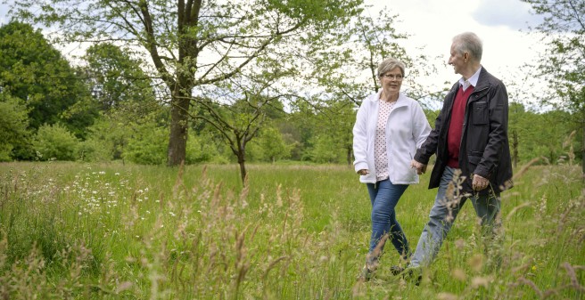 Peter Seifert und seine Frau gehen durch eine Wiese. Sie lächeln sich an, Peter Seifert schreitet kräftig aus.