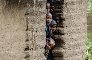 Einen Schar Kinder blickt neugierig aus der schmalen Tür einer Lehmhütte, sie stehen dicht gedrängt