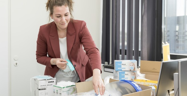 Vor Janna-Lynn Schröder liegen auf einem Schreibtisch sehr viele unterschiedliche Masken in verschiedenen Verpackungseinheiten. Sie greift nach einer davon