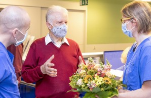 Peter Seifert bedankt sich bei dem Team aus der Intensivstation, sie stehen eng beieinander und tragen Atemschutzmasken. Dr. Sensen mit einem bunten Blumenstrauß in der Hand