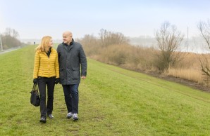 Prof. Barbara Schmalfeld und Mann spazieren auf dem Deich, sie blicken sich an