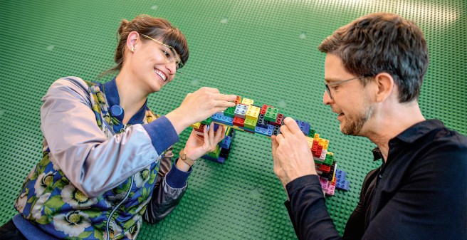 Eine Frau und ein Mann bauen eine Brücke aus Duplo-Steinen