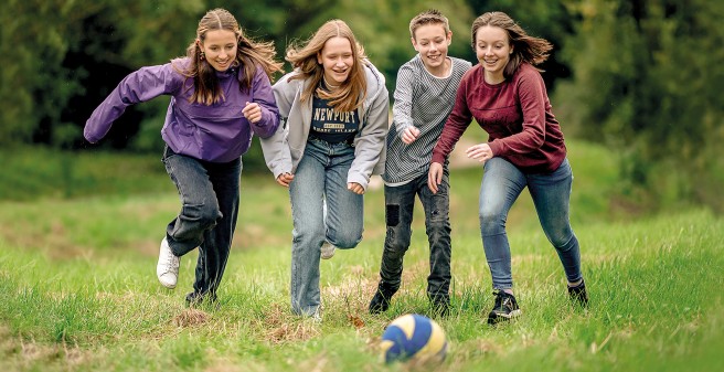 vier Jugendliche stürmen dicht gedrängt und lachend einem Ball hinterher